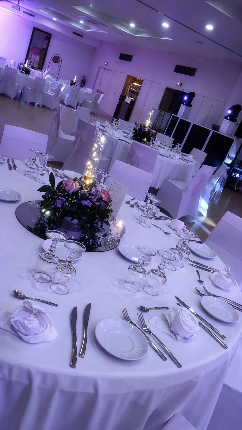 Salle de réception avec tables blanches dressées, bouquets et éclairages lilas